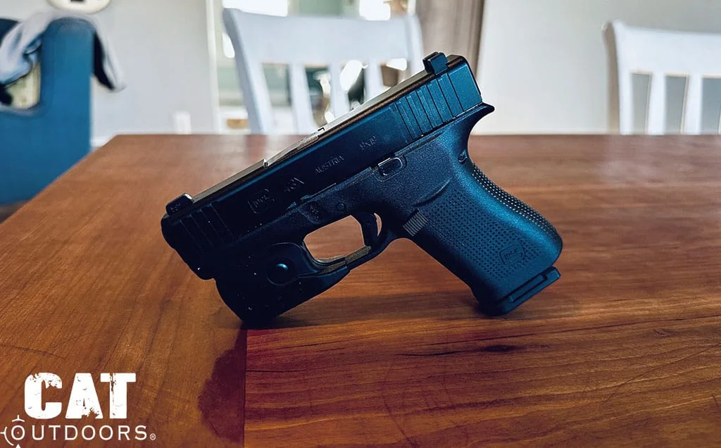 Side view of the Glock 43X with a trigger guard weapon light on a wooden dining table