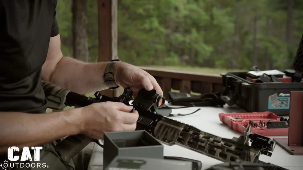 Hands seating the Romeo 5 on the AR-15 rail at a range table, its empty box in front