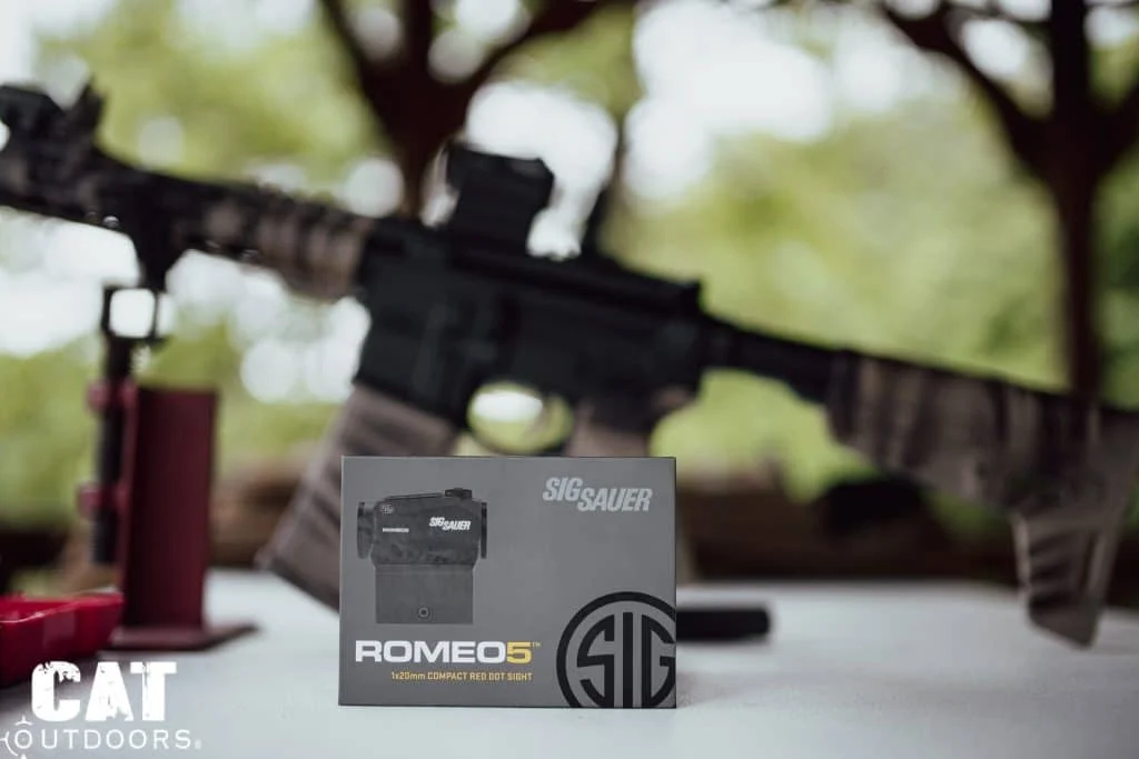 SIG Romeo 5 retail box in sharp focus on the range table, the camo AR-15 blurred behind it