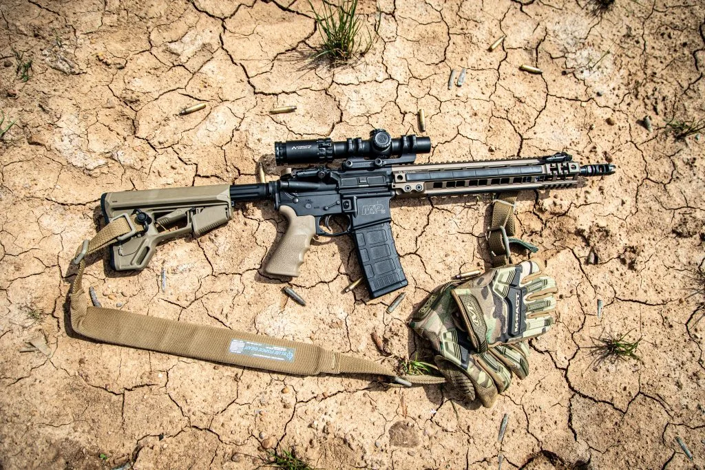 Primary Arms SLx 1-8x24 LPVO on an M&P15 lying on cracked dry dirt with spent brass and gloves