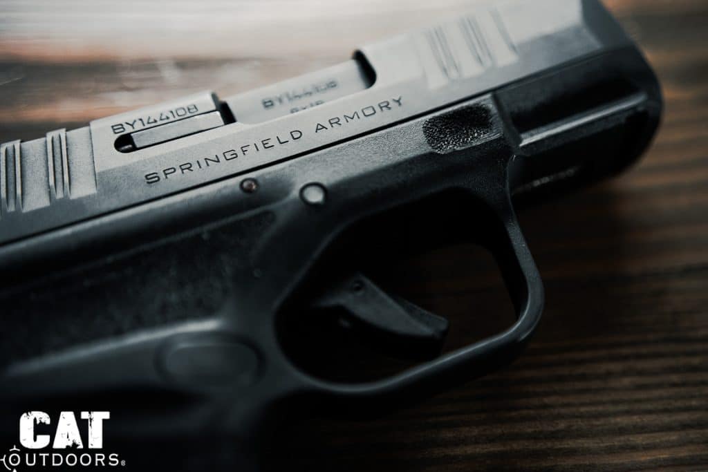 Left-side macro of the Springfield Hellcat showing serial number, Springfield Armory engraving, trigger blade safety, and Adaptive Grip Texture detail