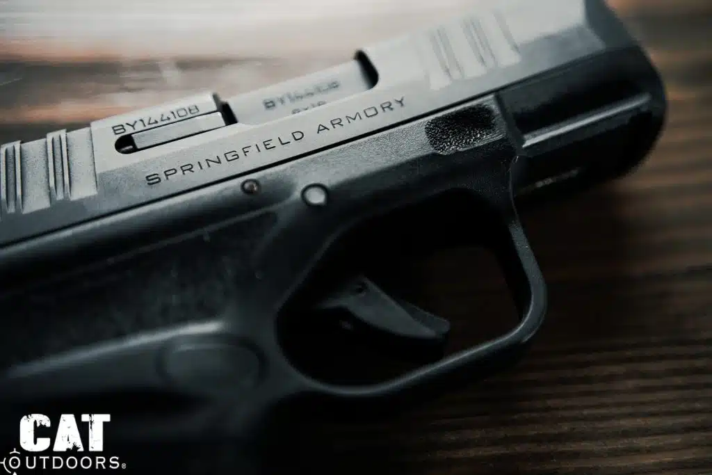 Left-side macro of the Springfield Hellcat showing serial number, Springfield Armory engraving, trigger blade safety, and Adaptive Grip Texture detail