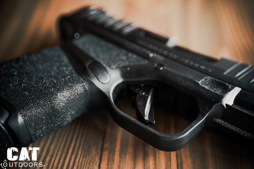 Macro close-up of the Springfield Hellcat flat-faced trigger with integrated blade safety and Adaptive Grip Texture in extreme detail