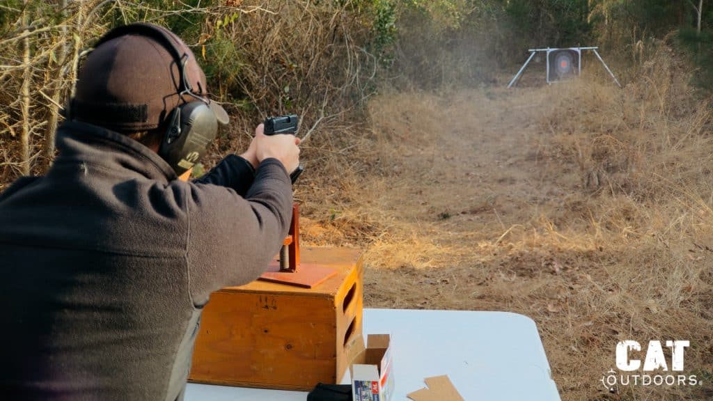 Brad firing the Springfield Hellcat from a seated bench rest position at an outdoor range with a target visible downrange