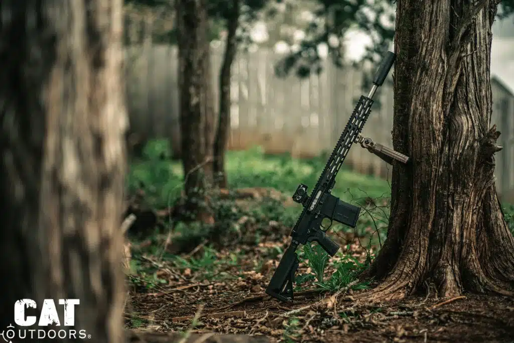 Suppressed AR-15 with CVLIFE bipod folded leaning against a tree in wooded setting