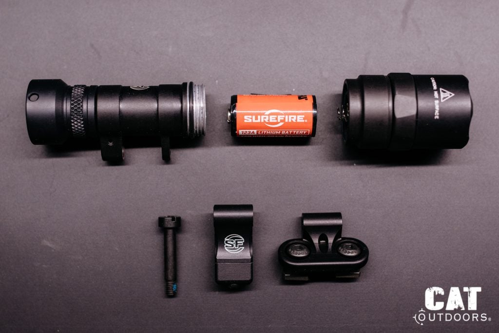 SureFire M340C-PRO Mini Scout Light Pro disassembled, showing light body, CR123A battery, tailcap, Picatinny adapter, M-LOK adapter, and pivot screw