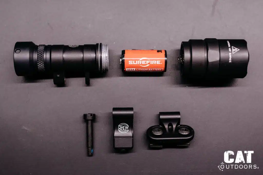 SureFire M340C-PRO Mini Scout Light Pro disassembled, showing light body, CR123A battery, tailcap, Picatinny adapter, M-LOK adapter, and pivot screw