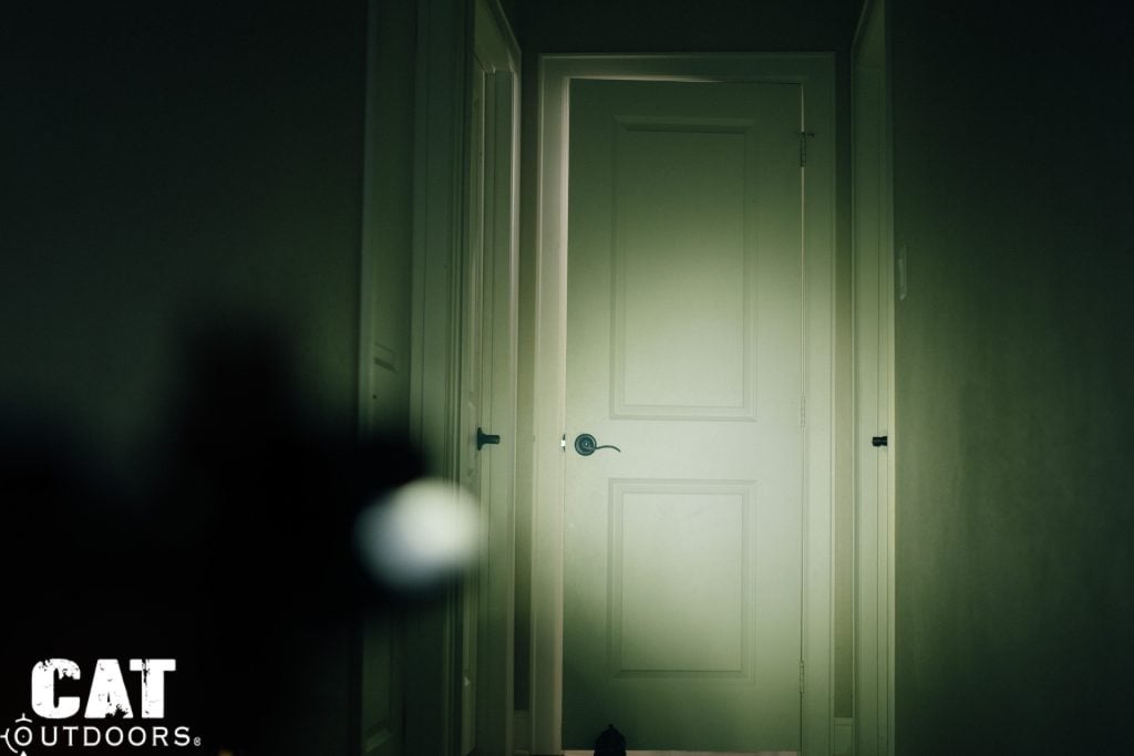 SureFire Mini Scout Light Pro illuminating a closed door at the end of a dark hallway, showing the TIR hybrid beam pattern with hot spot on the door and spill on the walls