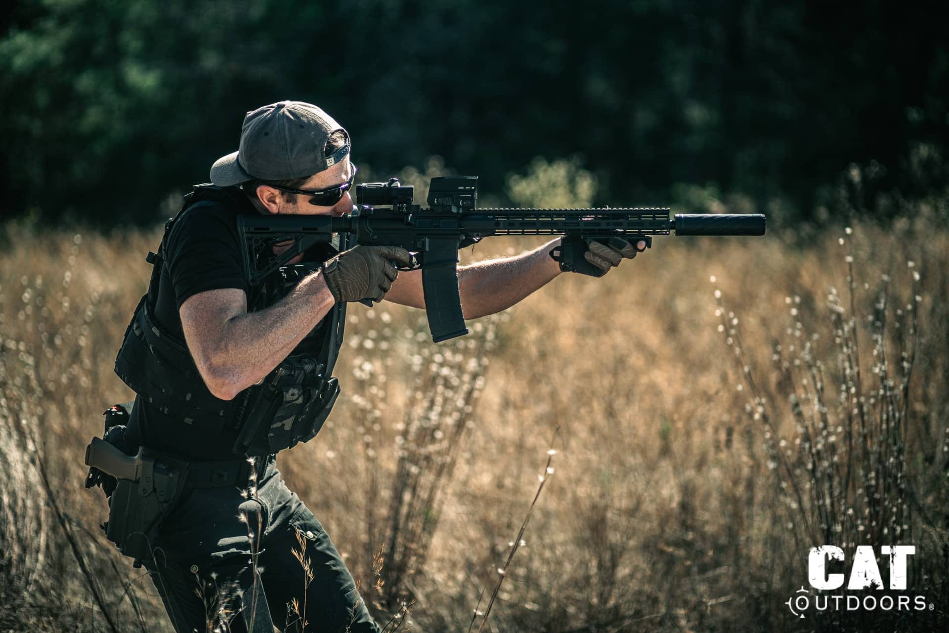 CAT Outdoors team member firing a suppressed AR rifle in a field, real-world testing conditions