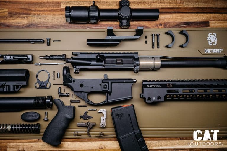 AR-15 rifle fully broken down into components — upper receiver, lower receiver, bolt carrier group, handguard, Vortex optic, trigger group, and magazine laid out on a build mat
