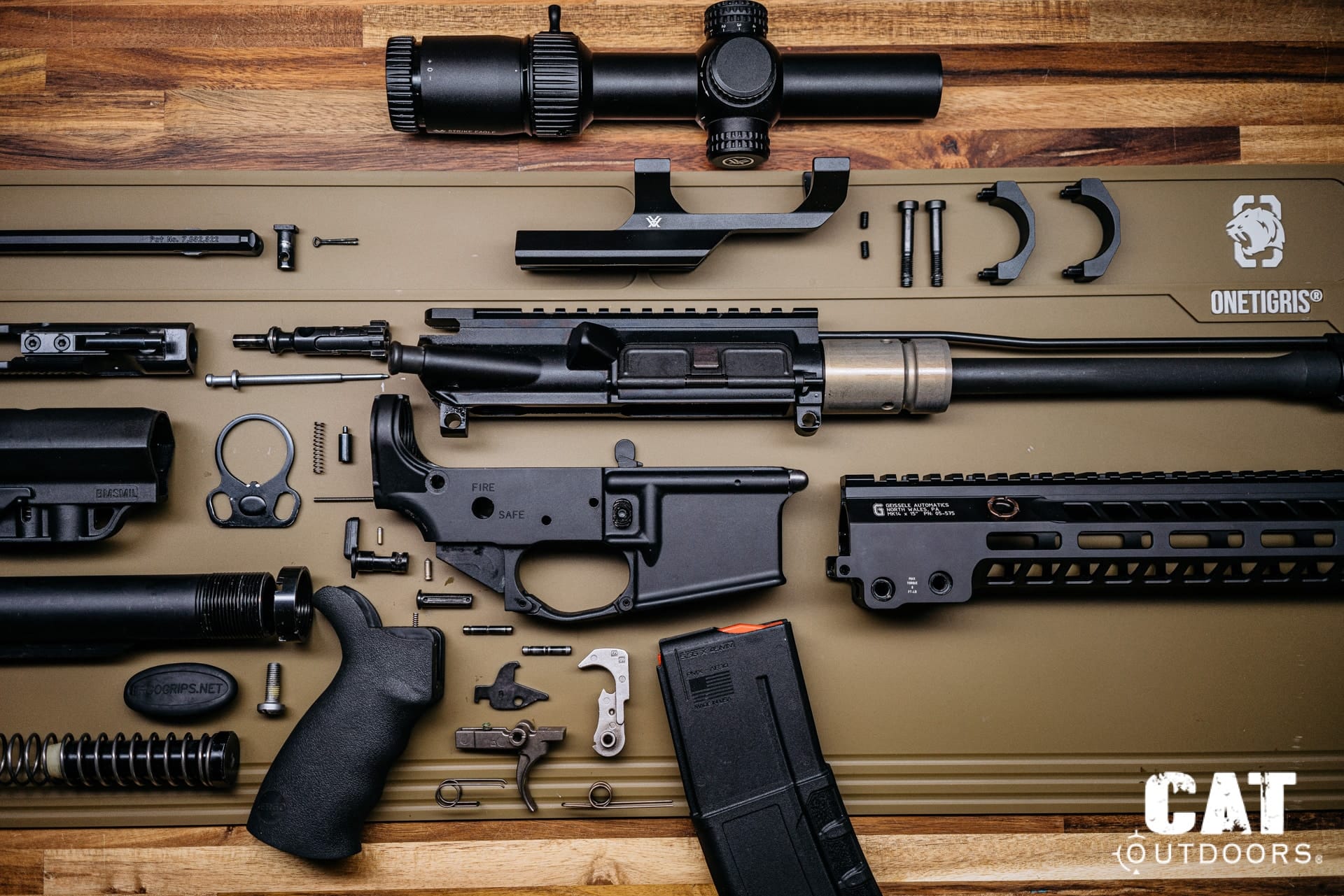 AR-15 rifle fully broken down into components — upper receiver, lower receiver, bolt carrier group, handguard, optic, and trigger assembly