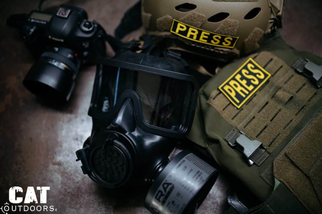 Mira Safety CM-8M beside a camera, helmet, and plate carrier with PRESS patches