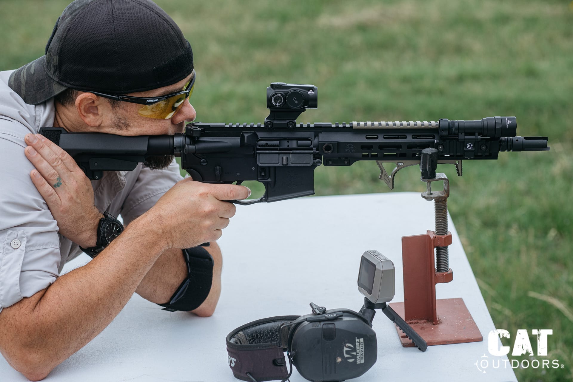 Brad benched behind the suppressed PSA Sabre with the Primary Arms GLx MD-21 mounted, shot timer and ear pro on the table