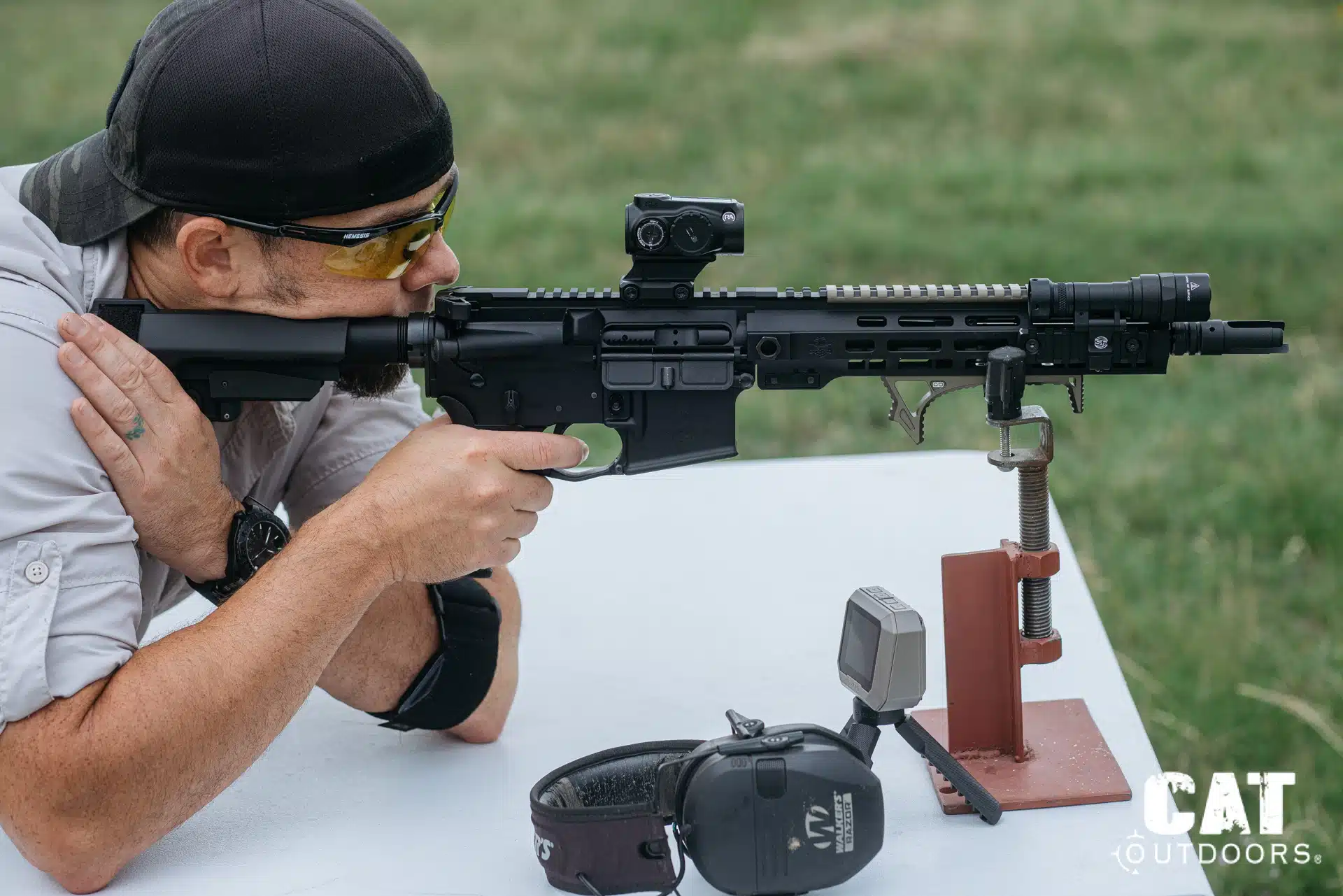Brad benched behind the suppressed PSA Sabre with the Primary Arms GLx MD-21 mounted, shot timer and ear pro on the table