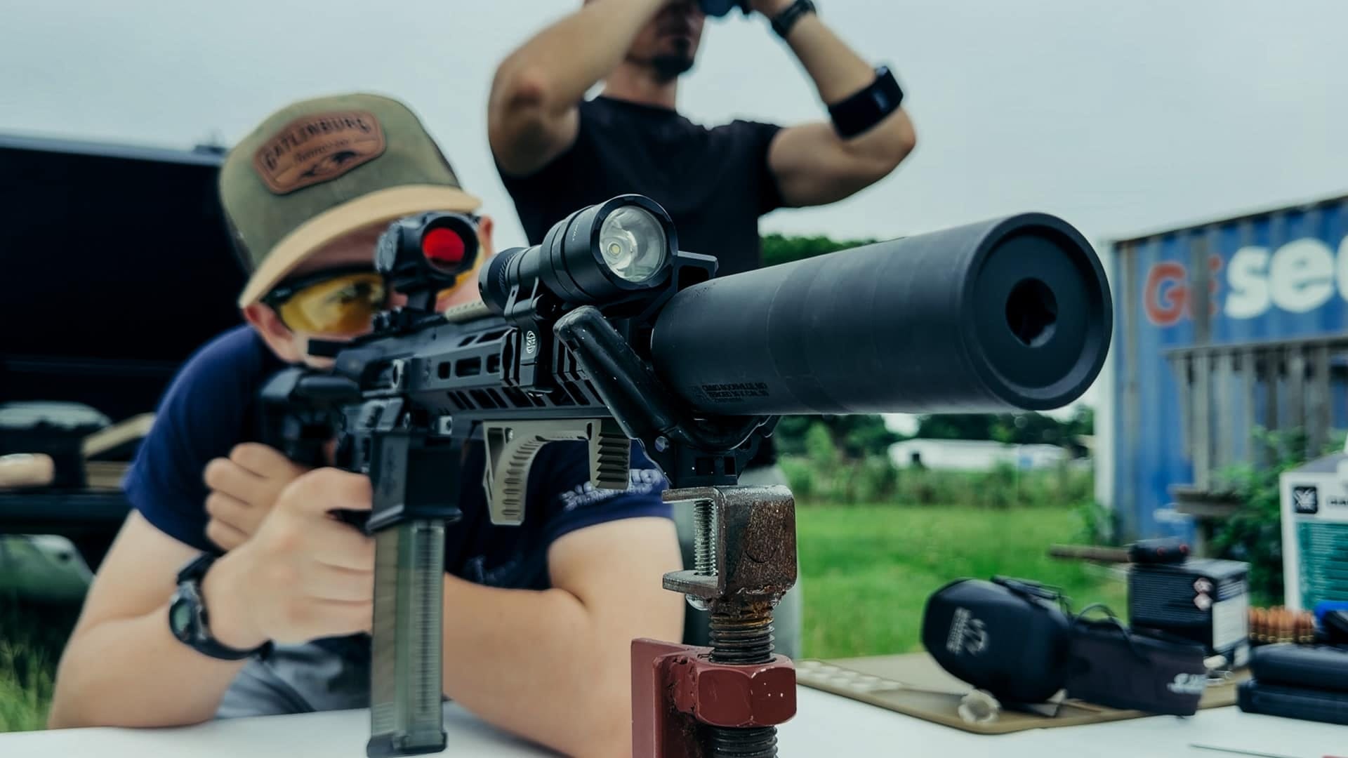 New shooter behind the suppressed 300 Blackout with the GLx MD-21 dot glowing, spotter watching through binoculars