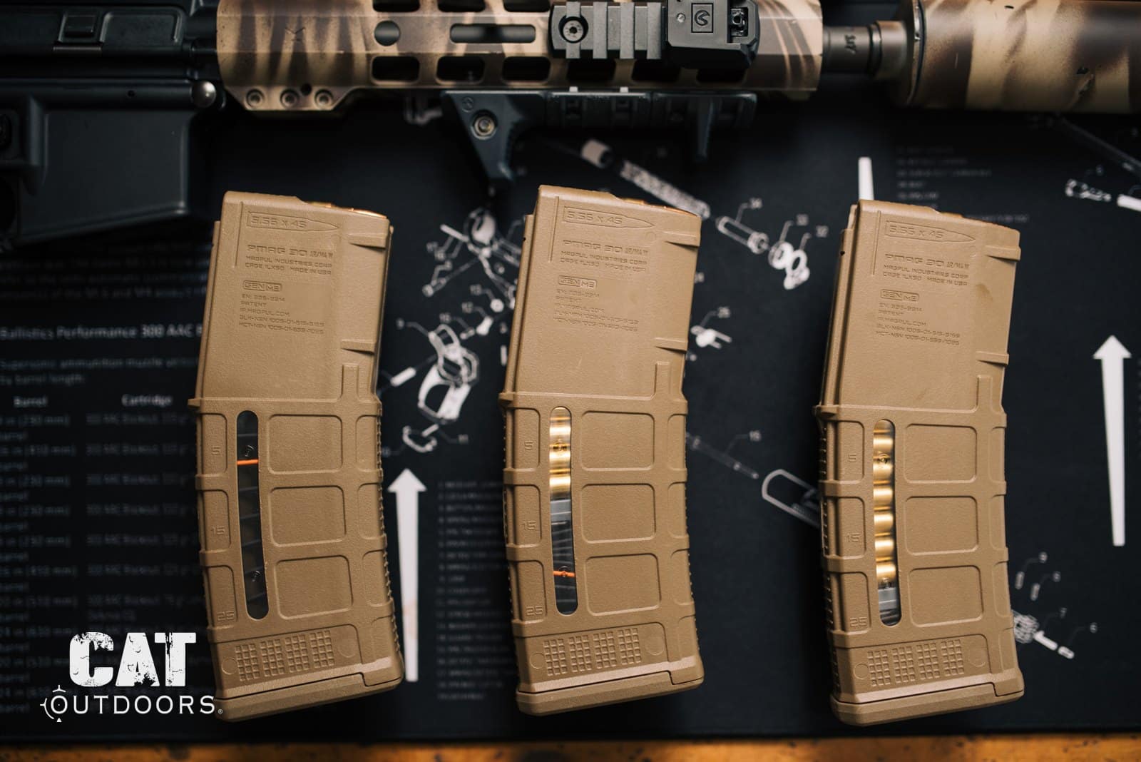 Three Magpul PMAG 30-round AR-15 magazines lined up on a workbench mat below a rifle