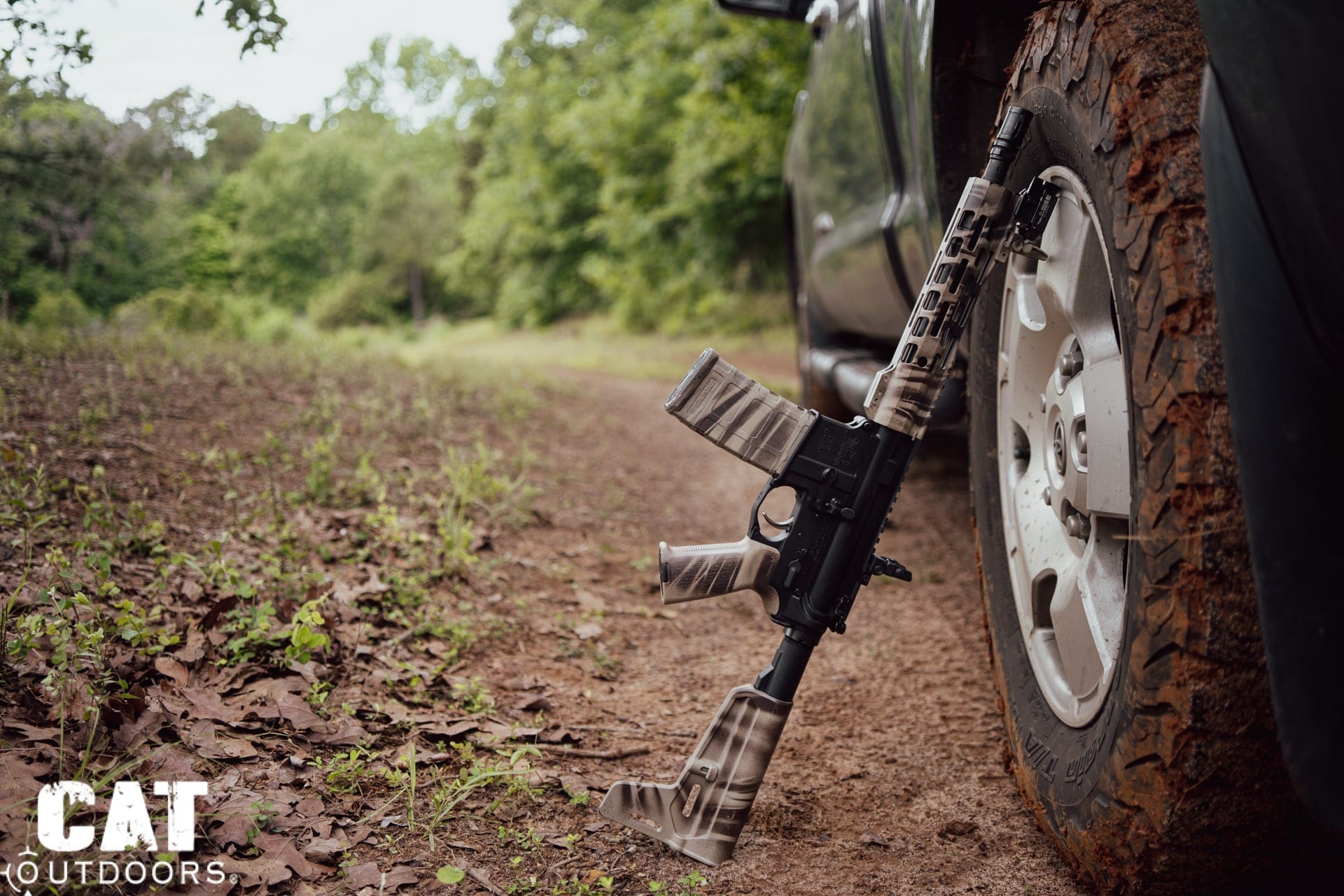 Braced AR pistol leaning against a muddy truck tire on a wooded trail, inches from being an SBR on paper
