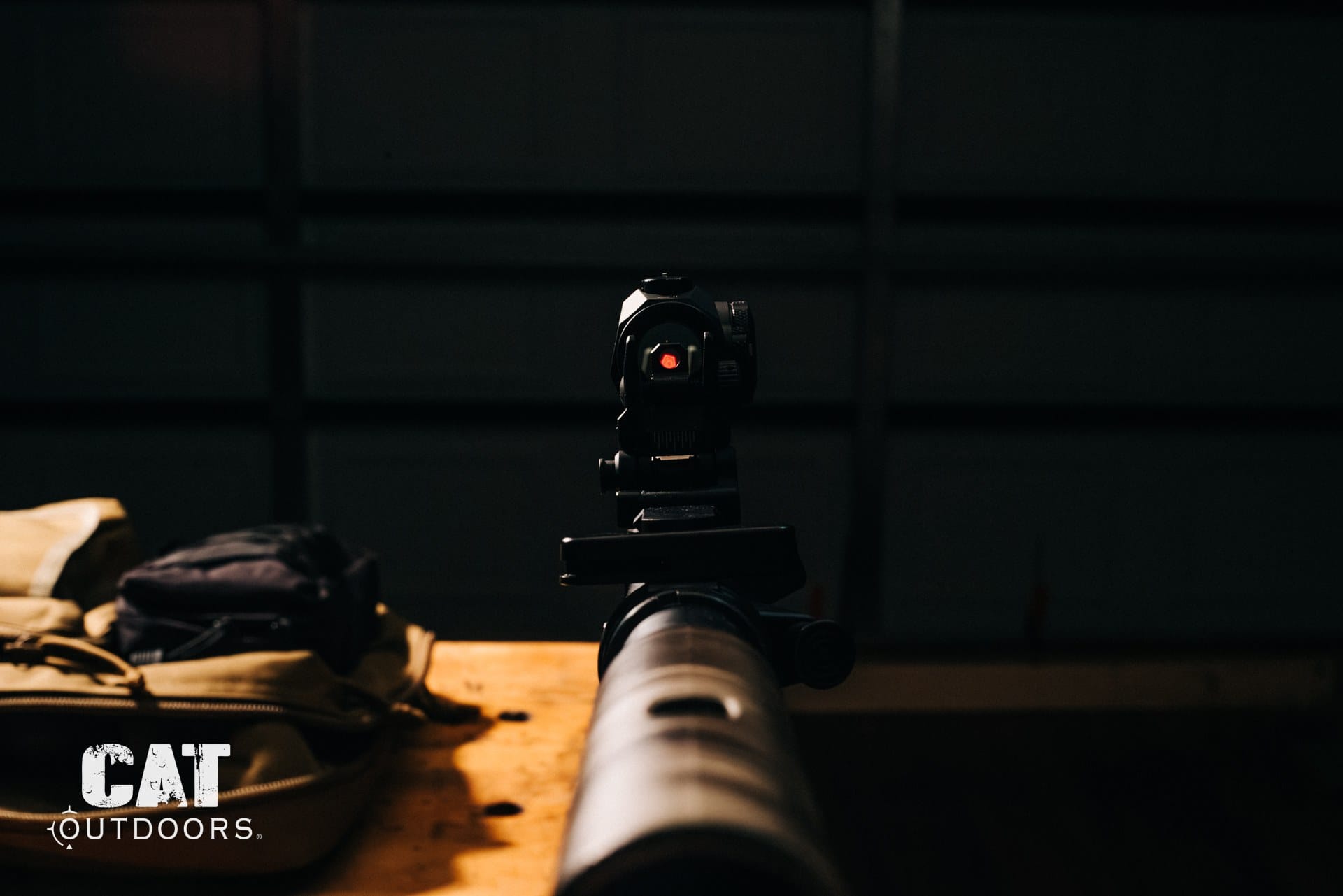 Suppressed AR-15 on a workbench, muzzle-on view behind a red dot sight