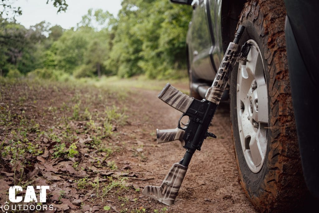 Camo AR pistol with a stabilizing brace leaning against a truck tire