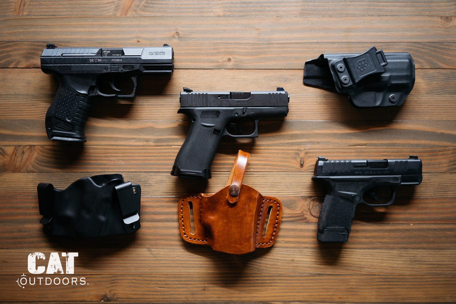 Three concealed carry pistols with holsters on a wood table