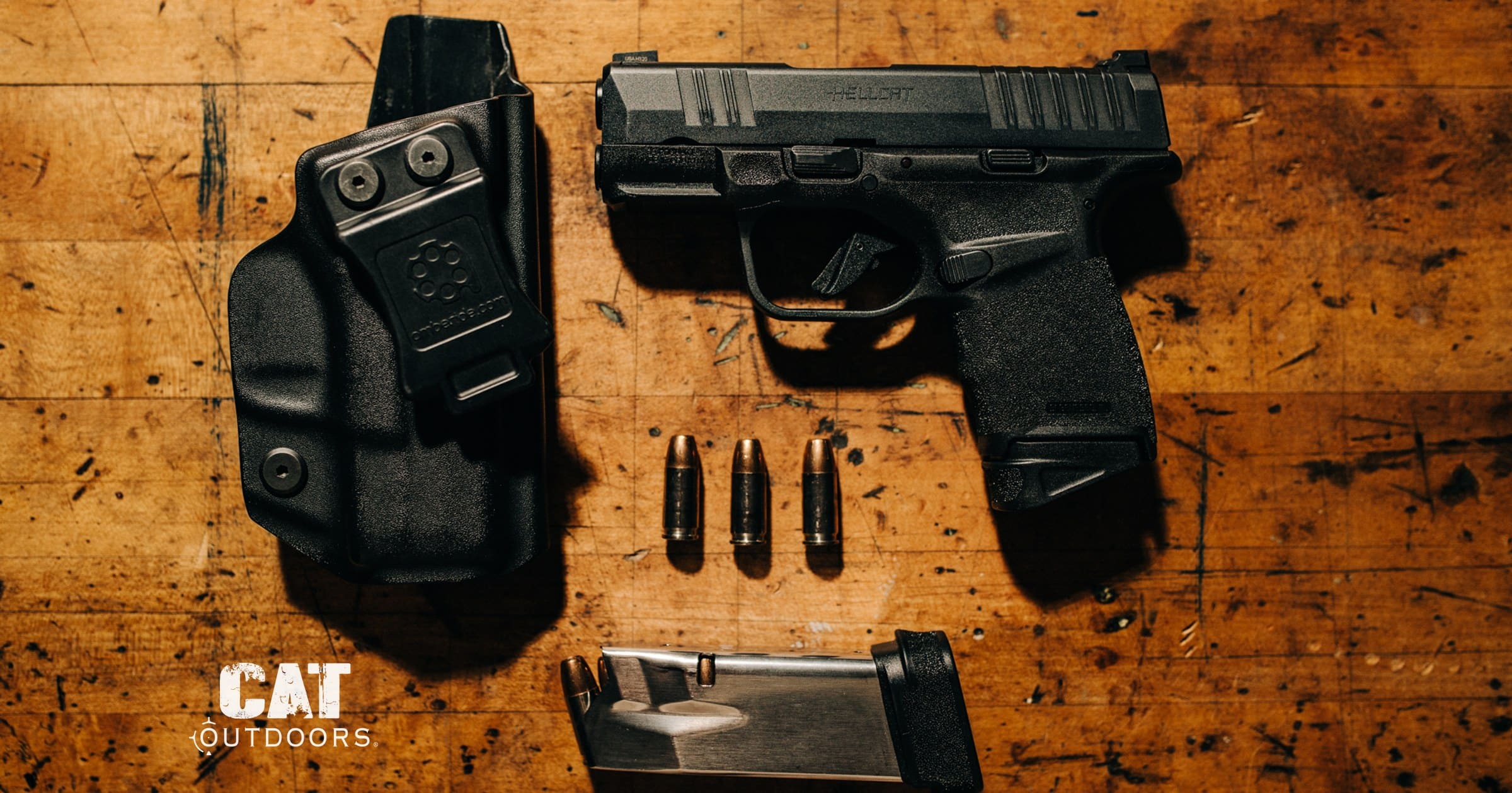 Springfield Hellcat 9mm pistol with IWB holster, spare magazine, and 9mm rounds on a workbench