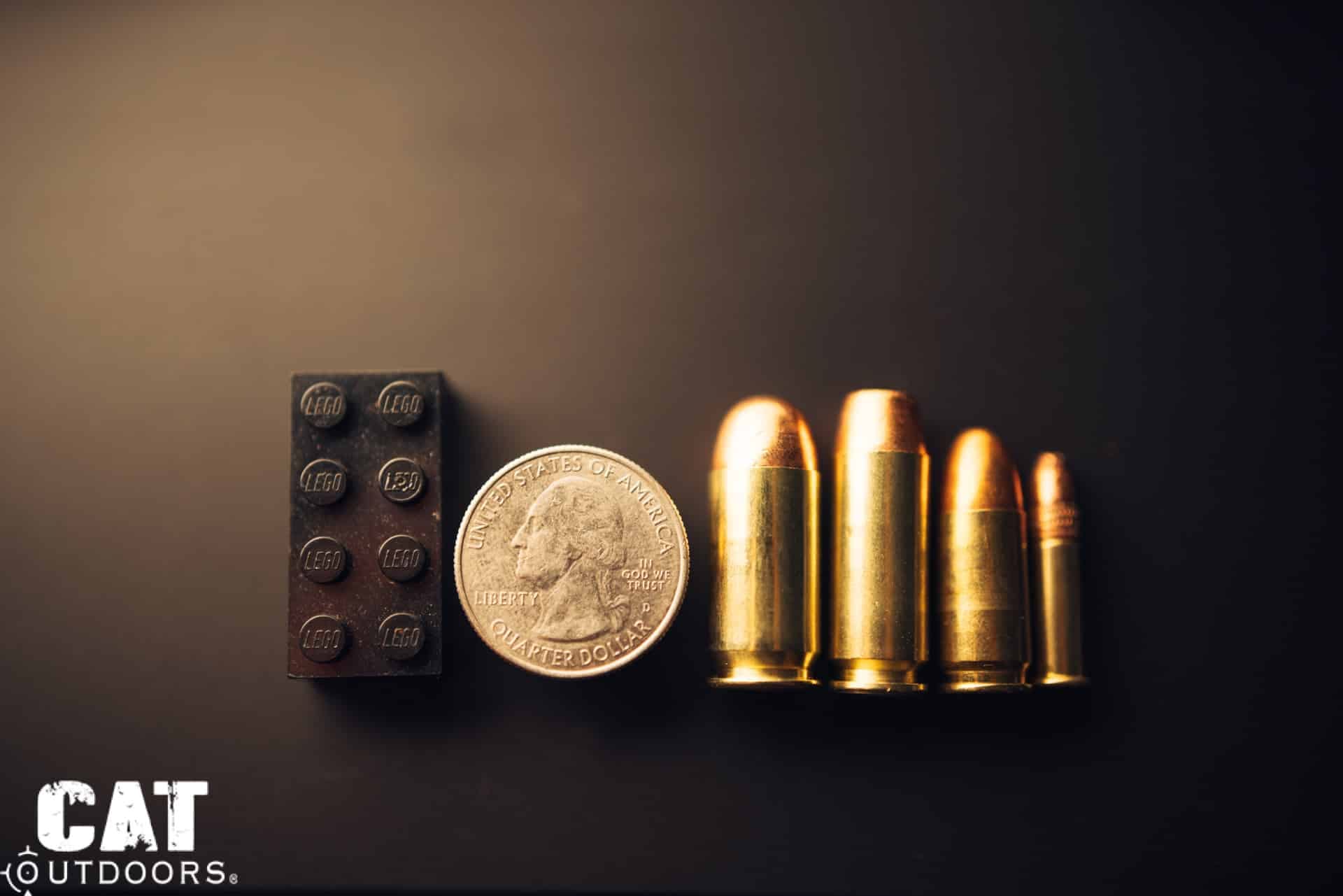 Four pistol cartridges lined up next to a quarter and a Lego brick for scale