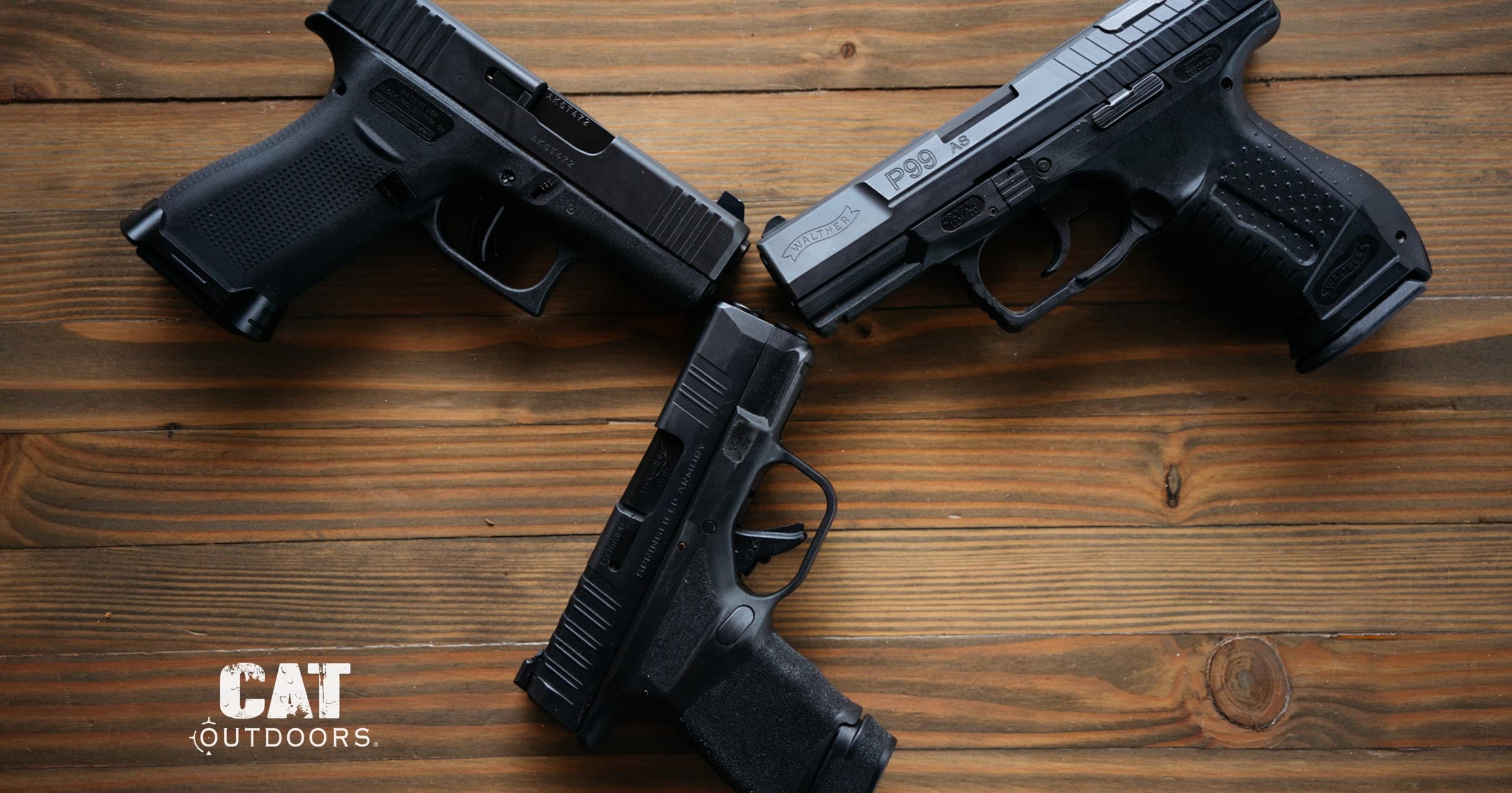 Glock 44, Walther P99, and Springfield Hellcat semiautomatic pistols on a wood table