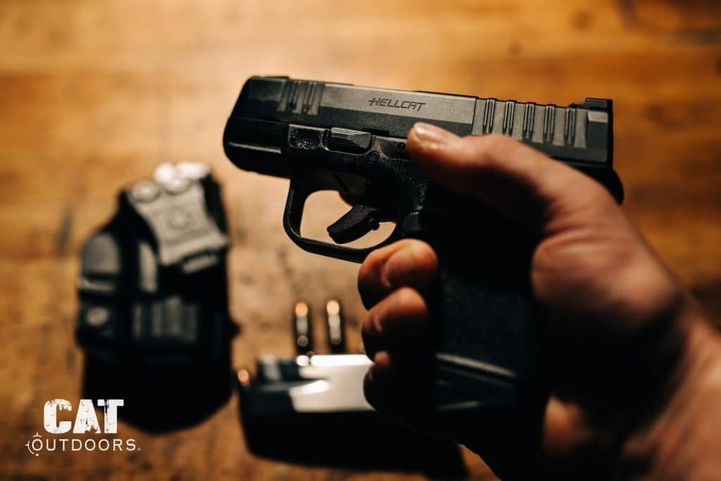 Springfield Hellcat 9mm held in hand with holster and spare magazine in the background