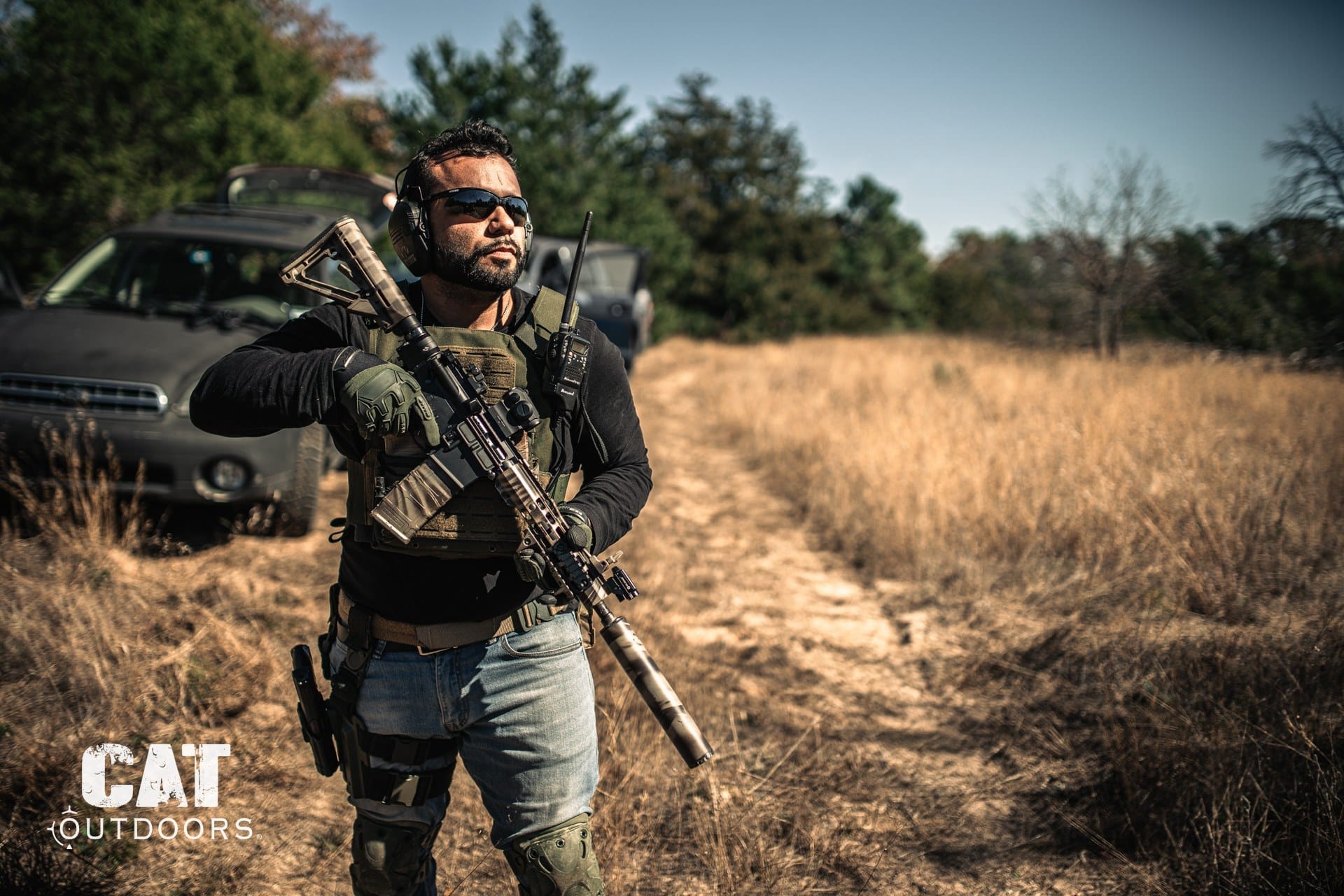 Shooter carrying a suppressed AR-15 in a field