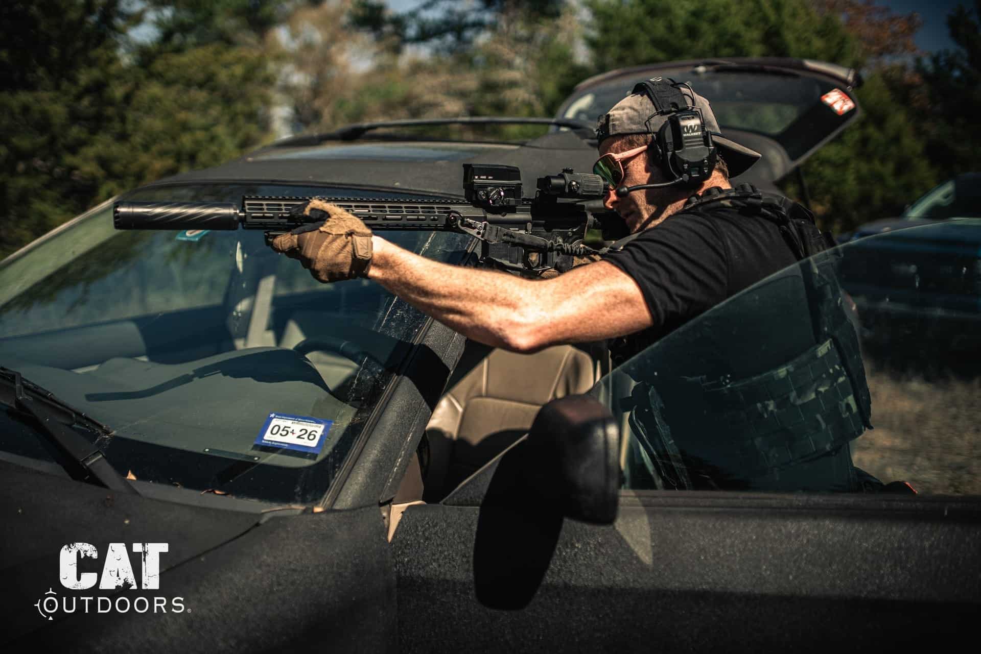 Shooter firing a suppressed AR-15 over a car hood