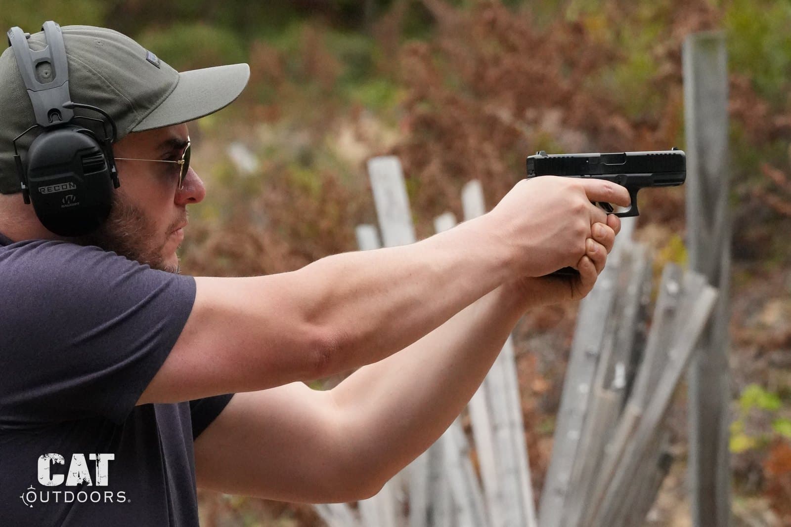 Shooting the Glock 19 Gen 5 two-handed at a blue barrel target with eye and ear protection on