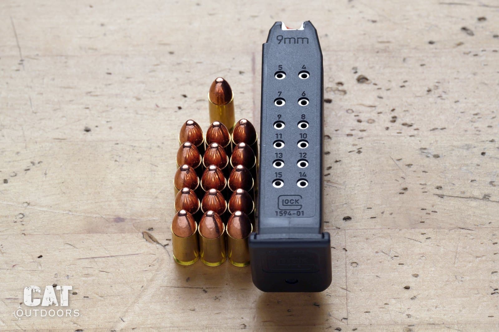 Glock factory 15-round magazine with numbered witness holes beside fifteen 9mm rounds