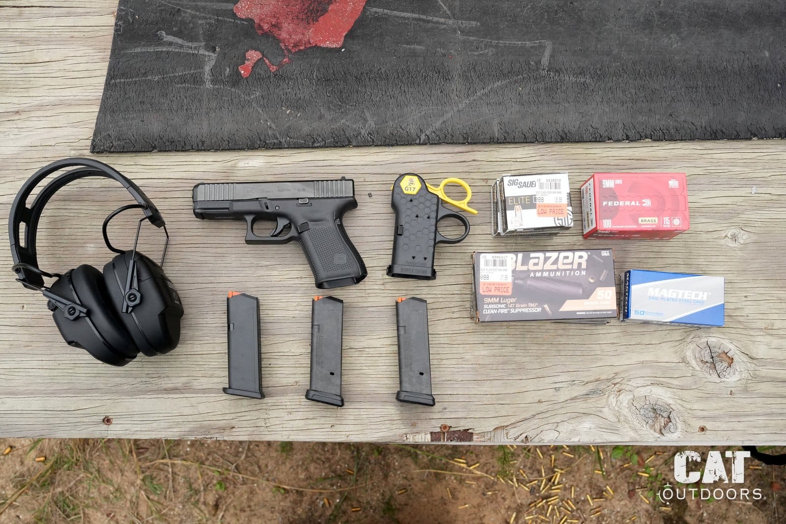 Range bench flat lay with the Speed Beez loader, Glock 19, magazines, ammo boxes and ear protection