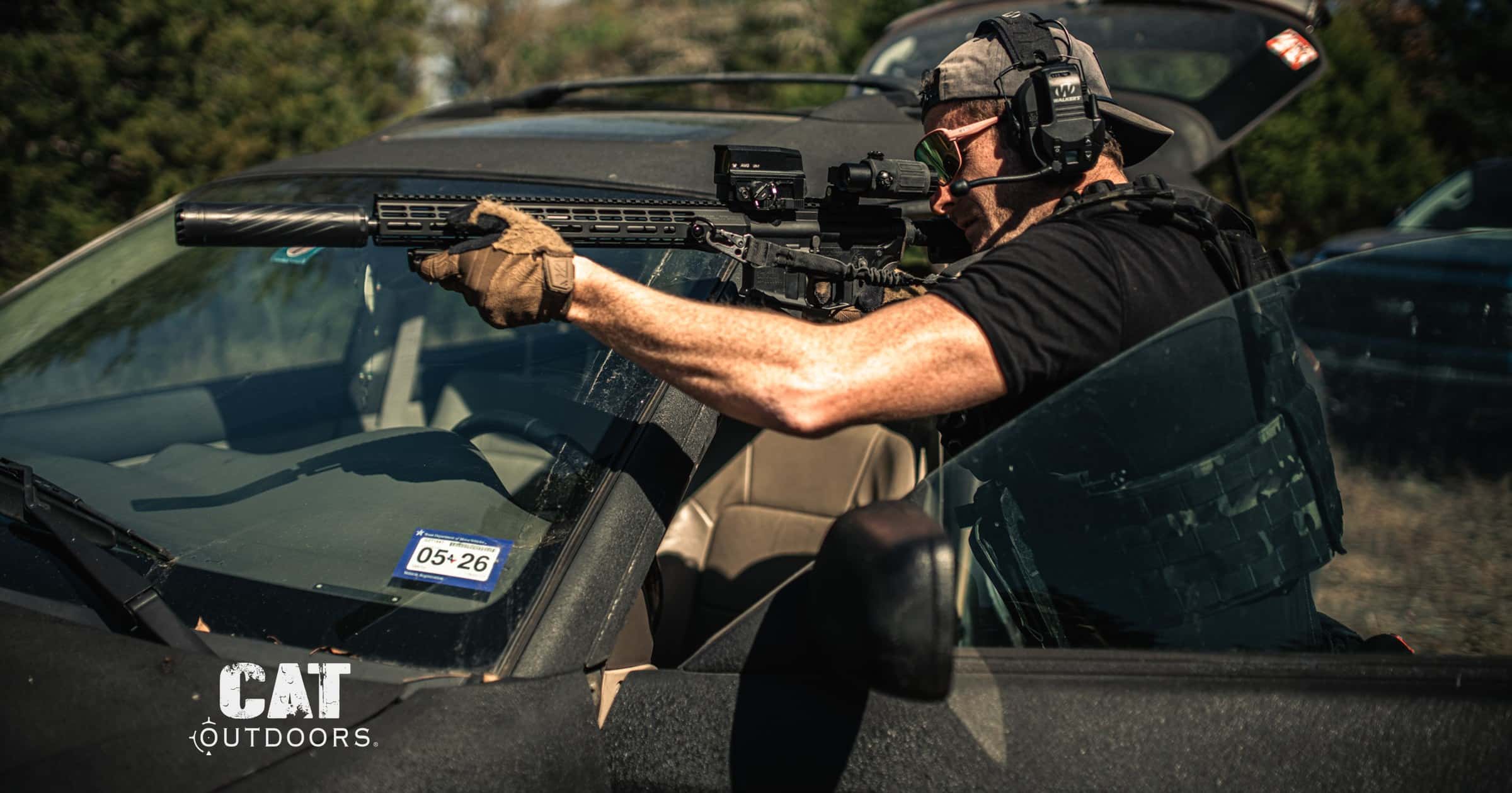 Shooter fires a suppressed AR-15 over the hood of a car during a training drill