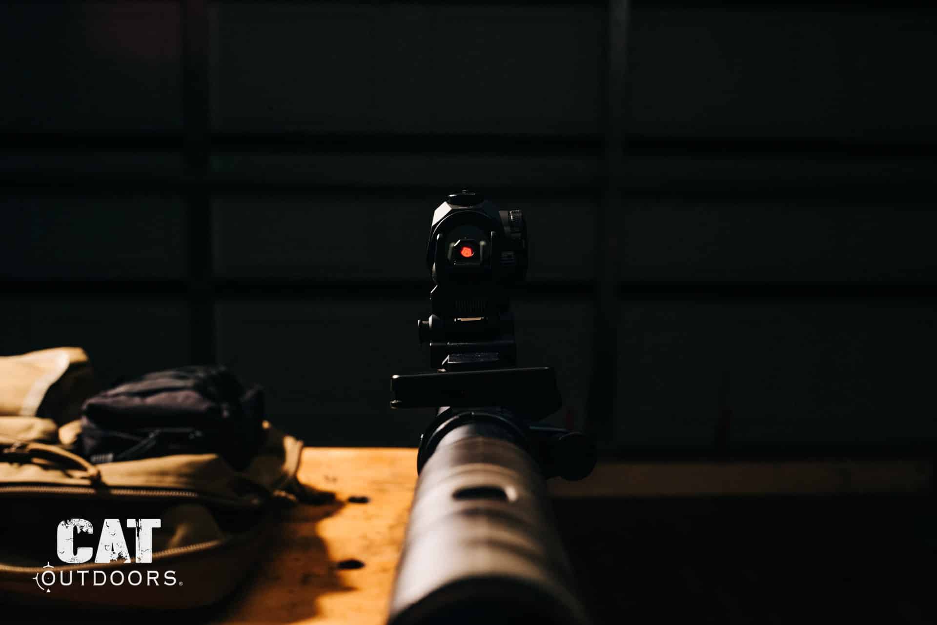 Rifle suppressor and red dot sight on a workbench in low light