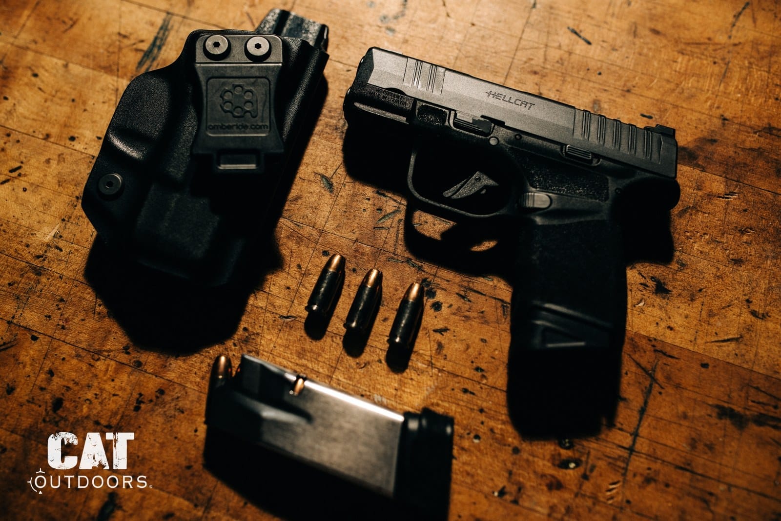 Springfield Hellcat pistol with IWB holster, spare magazine, and 9mm rounds on a workbench