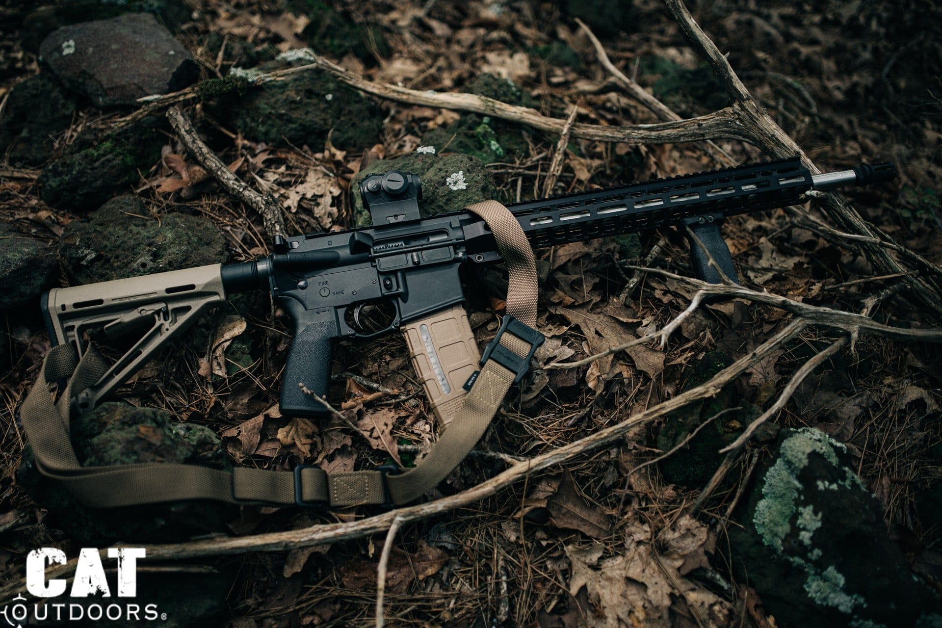 AR-15 rifle with a red dot optic and two-point sling resting on the forest floor