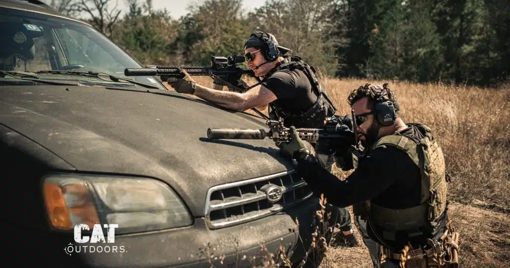 Two shooters firing suppressed AR-15 rifles over the hood of a car