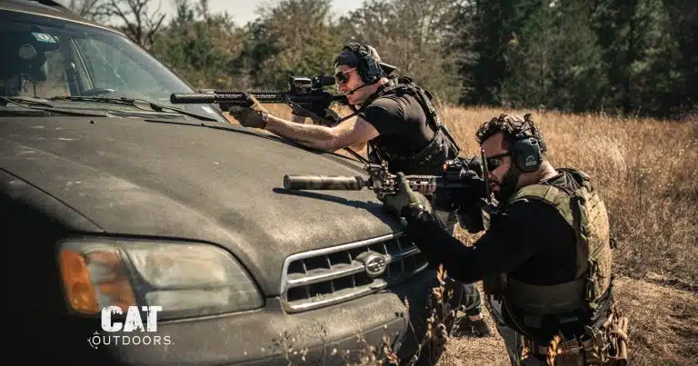 Two shooters firing suppressed AR-15 rifles over the hood of a car